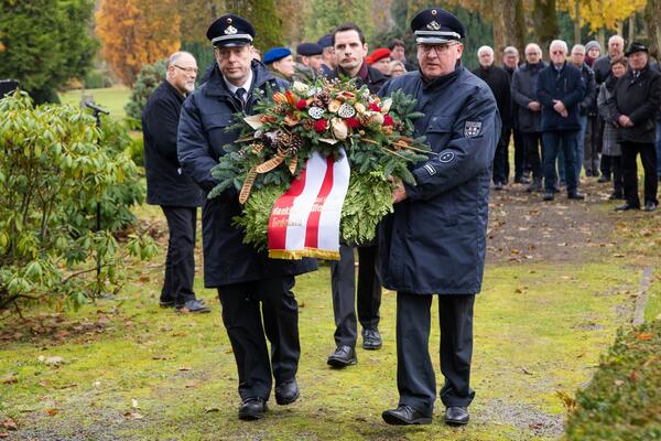 Bild vergr&ouml;&szlig;ern: Mehrere Menschen mit einem Gedenkkranz.