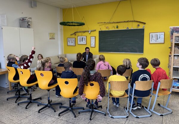 Bild vergr&ouml;&szlig;ern: Ein Mann liest einer Schulklasse vor.