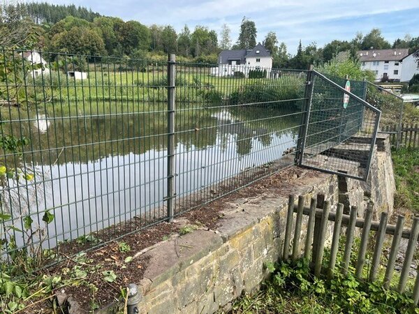 Blick durch einen Zaun auf einen kleinen Teich